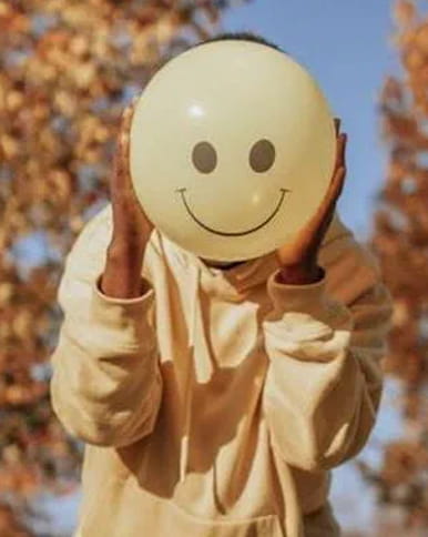 A person holding up a balloon with a smiley face on it