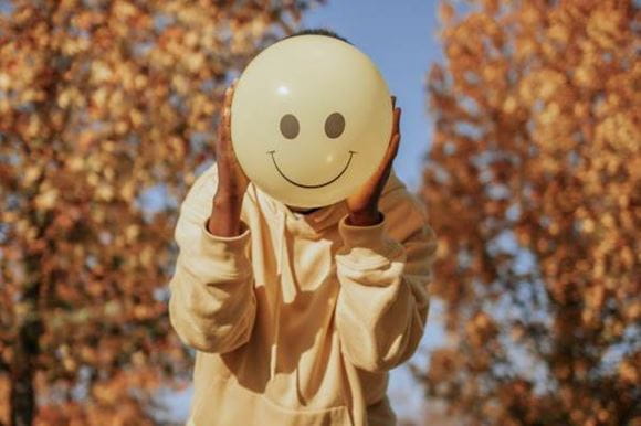 A woman holding a yellow balloon with a smiley face on it